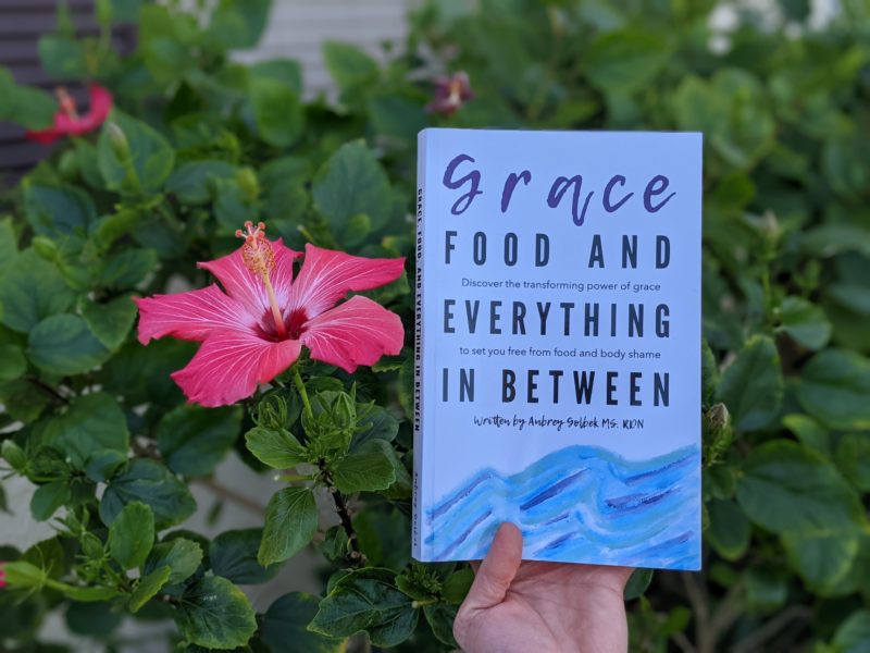 The best books about food and faith Erin holding her pick for the best intuitive eating books Grace Food and Everything in Between by Aubrey Golbek